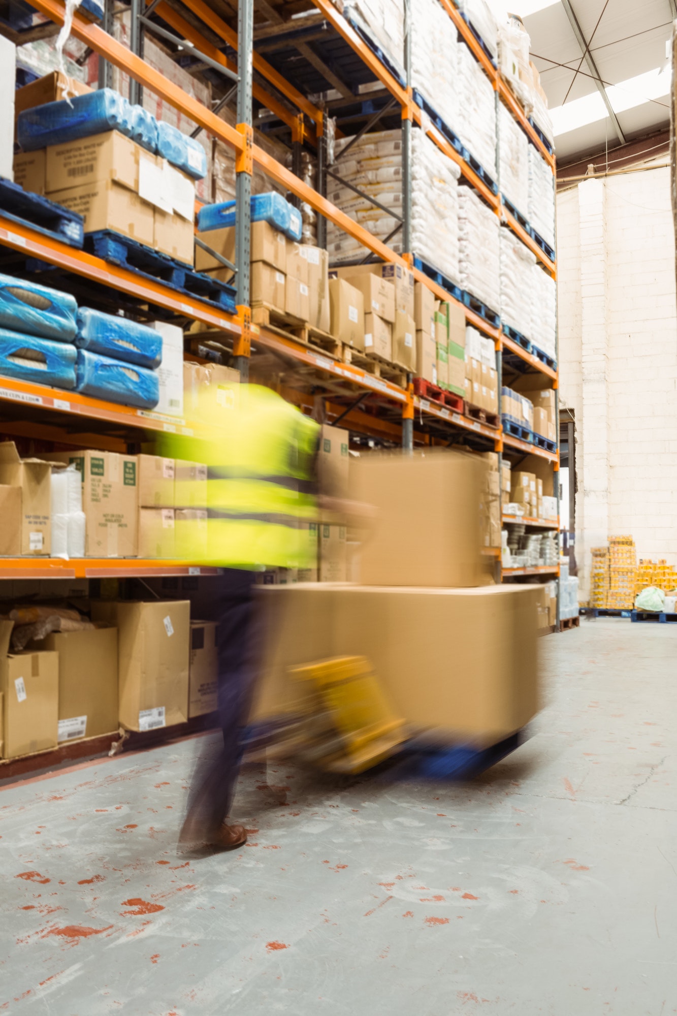 Worker pushing trolley with boxes in a blur in a large warehouse